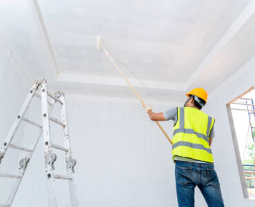 Rear view of asian painter man painting the wall, with paint roller and bucket in an unfinished house, Construction work, isolated on big empty space with ladder