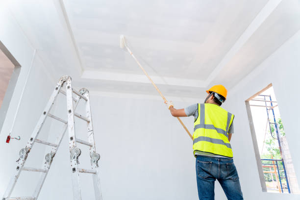 Rear view of asian painter man painting the wall, with paint roller and bucket in an unfinished house, Construction work, isolated on big empty space with ladder