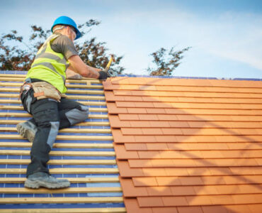 a roofer nails on the roof tiles