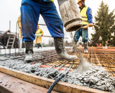 Manual workers pouring cement through pipe on roof.